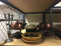 Overall view of the fondue set including two hammered copper pots on metal stands, ceramic bowls stacked behind, and the fork holder with forks.