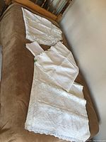 Full view of the vintage white linen tablecloth and three matching napkins laid out on a bed, showcasing overall size and lace detailing.