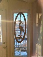Wood heron wall hanging in front of a window with natural daylight showing its silhouette and general shape.