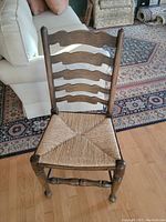 Front view showing woven straw seat and wooden ladder back with curved horizontal slats and turned legs.