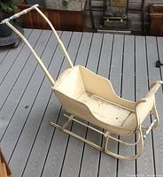 Side angled view of the antique wooden child's push sleigh on a deck showing wear and paint chipping.