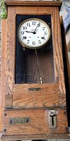 Front view of oak cabinet clock with glass door, white painted face with black numerals, and brass pendulum visible below.