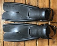 Pair of black Apollo Bio Fin Pro split scuba dive fins laid side by side on wood floor, showing top view and embossed logos.