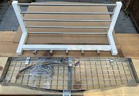 Both racks visible on a cardboard surface. White IKEA wood rack with horizontal metal bars and hooks. Chrome steel grid rack with multiple hooks wrapped in plastic.