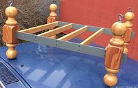 Metal and wood hanging pot rack with turned wooden posts and hooks, placed on blue surface outdoors.