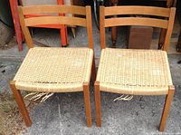 Pair of vintage J.L. Møller chairs showing wooden frames and woven seats with broken fibers and discoloration.