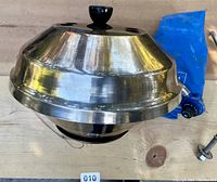 Top view of MAGMA stainless steel marine BBQ grill dome lid with black knob and blue carry bag partially visible.