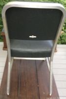 Back view of one vintage aluminum framed chair with black vinyl upholstery, showing intact vinyl and aluminum frame.