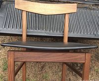 Single chair front view showing floating black vinyl seat and walnut frame.