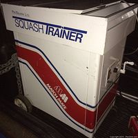 Side view of ProSquash Match Mate squash ball training machine showing white and red metal cabinet with blue and red decals and branding.