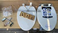 Full lot displayed on wood plank surface including two toilet seats, one sealed, three towel racks including teak and chrome, chromed brass toilet paper holder with hardware.