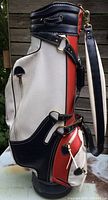 Side view of the vintage golf bag in white, navy blue and red leather with adjustable blue straps.