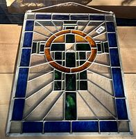 Front side of the entire leaded glass panel showing the cross inside an amber circle with blue border and various clear textured glass pieces.