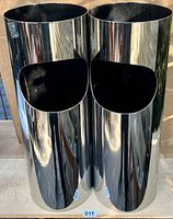 Front view of two vintage chrome on steel waste cans showing cylindrical shape and open oval front disposal area, reflective chrome exterior with some wear and spots with missing chrome on rear.