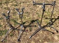 Four drum stands positioned on grass including three Yamaha stands and one unbranded stand.