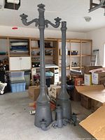Two assembled lamp post shafts and detached fixtures arranged in garage interior