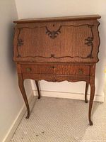 Full view of the wooden secretary desk showing front carved panel, drawer, and slender legs.
