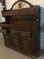 Front view of dark wood cabinet with stained glass floral panel and multiple drawers.