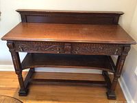 Overall front view of the wood sideboard showing the carved drawer, lower shelf, and backboard.
