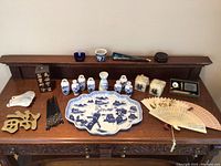 Overview of lot including carved stone sculpture, decorative porcelain, brass ornaments, fans, chopsticks, and other small items on wooden surface