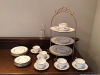 Full view of the Birks china set arranged on a wooden surface including stacked plates, cups, saucers, and the gold metal tiered stand.