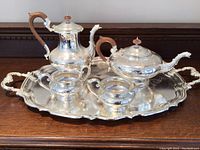 Full view of all five pieces on wooden surface, showing teapot, kettle, sugar bowl, cream pitcher, and serving tray together.