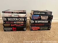 Two stacks of Stephen King hardcover books arranged upright on carpeted floor for display.