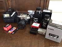 Overall photo of Canon camera, three lenses, accessories, and camera bag on wooden surface