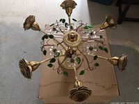 Top view of a floral metal chandelier showing gold-tone rose-shaped arms with clear flower and green leaf decorations on a circular frame.
