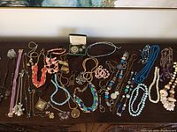 Wide shot of assortment of costume jewelry including necklaces, bracelets and earrings spread out on a wooden surface.