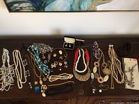 Wide view of the costume jewelry collection including necklaces and earrings laid out on a table, showing variety of styles and colors mostly in white, turquoise, black, and gold tones.