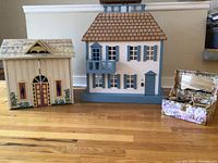 Two wooden doll houses next to a perforated decorative storage box on hardwood floor.