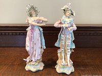 Front view of both figurines showing detailed clothing and bases on wooden surface.