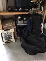 Overall view of Titleist golf bag leaning against shelving with clubs, headcovers and towel.