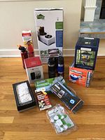 Full view of all household items in the lot arranged on floor including pet feeder, fire extinguishers, holiday frame, cleaning products, keyboard, and lantern.