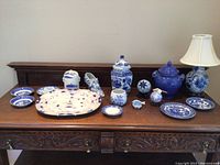 Front view of entire blue and white porcelain collection including lamp, jars, plates, decorative balls, shoe, dishes, and platter displayed on wooden table.
