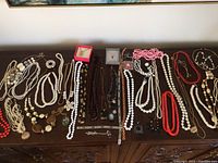 Overview of all costume jewelry items spread out on a wooden dresser including necklaces, bracelets, and brooches in various colors and styles.