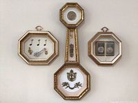 Full view of three framed decorative art pieces arranged on a white wall, showing one elongated frame with charms and two octagonal frames with illustrations.