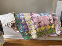 Vintage patchwork quilts and miscellaneous linens displayed over a white surface showing patterns and textiles.