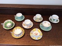 Eight vintage tea cups with their matching saucers of various floral and ornate designs arranged on a wooden surface.