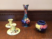 Frontal image of the lot showing Moorcroft tall vase, small round vase, and Grimwades candlesticks on wood surface