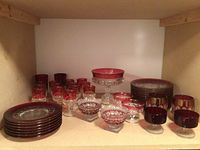 Wide view of the entire collection showing a mix of red and clear glass pieces including plates, glasses, footed bowls, and a pedestal dish.
