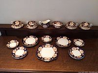 Full display of the Royal Albert china set including teacups, saucers, plates, and a cream pitcher with cobalt blue, floral, and gold pattern.