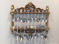 Full view of gold-toned ornate spoon rack holding 22 assorted decorative spoons hanging from two levels