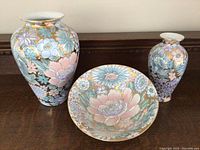 Front view of two tall vases and bowl showing detailed floral designs and gold accents