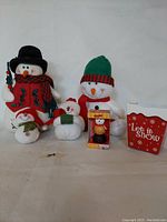 Photo showing all five snowman decorations including the large black-hatted snowman, medium green-red hat snowman, smaller snowmen, and Tim Hortons Timbits ornament with holiday gift bag.