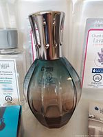 Close-up of the fragrance lamp with gradient green-brown glass and silver vented top.