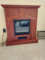 Full view of electric fireplace with medium wood tone wooden mantel and black framed glass front.