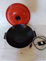 Photo of red electric wok with black cooking surface and red lid with knob, power cord and temperature control shown
