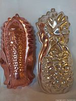 Photo of copper fish-shaped Jello mould and silver pineapple-shaped Jello mould showing detail and finish.